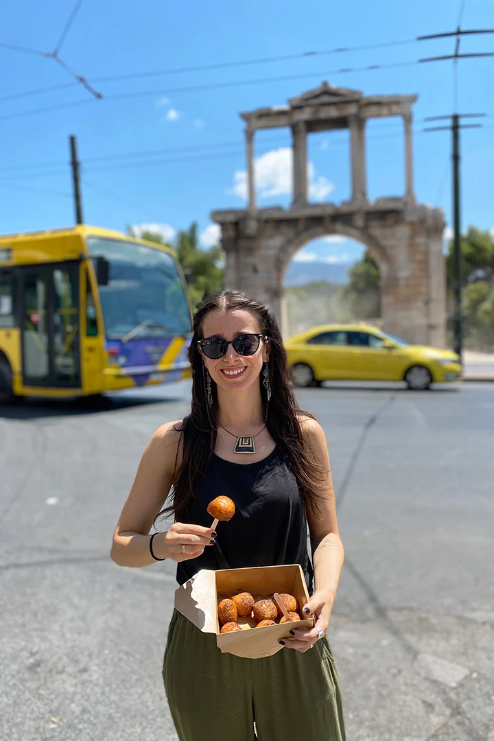 Woman eating loukoumades in front of Hadrian's arch in Athens Greece