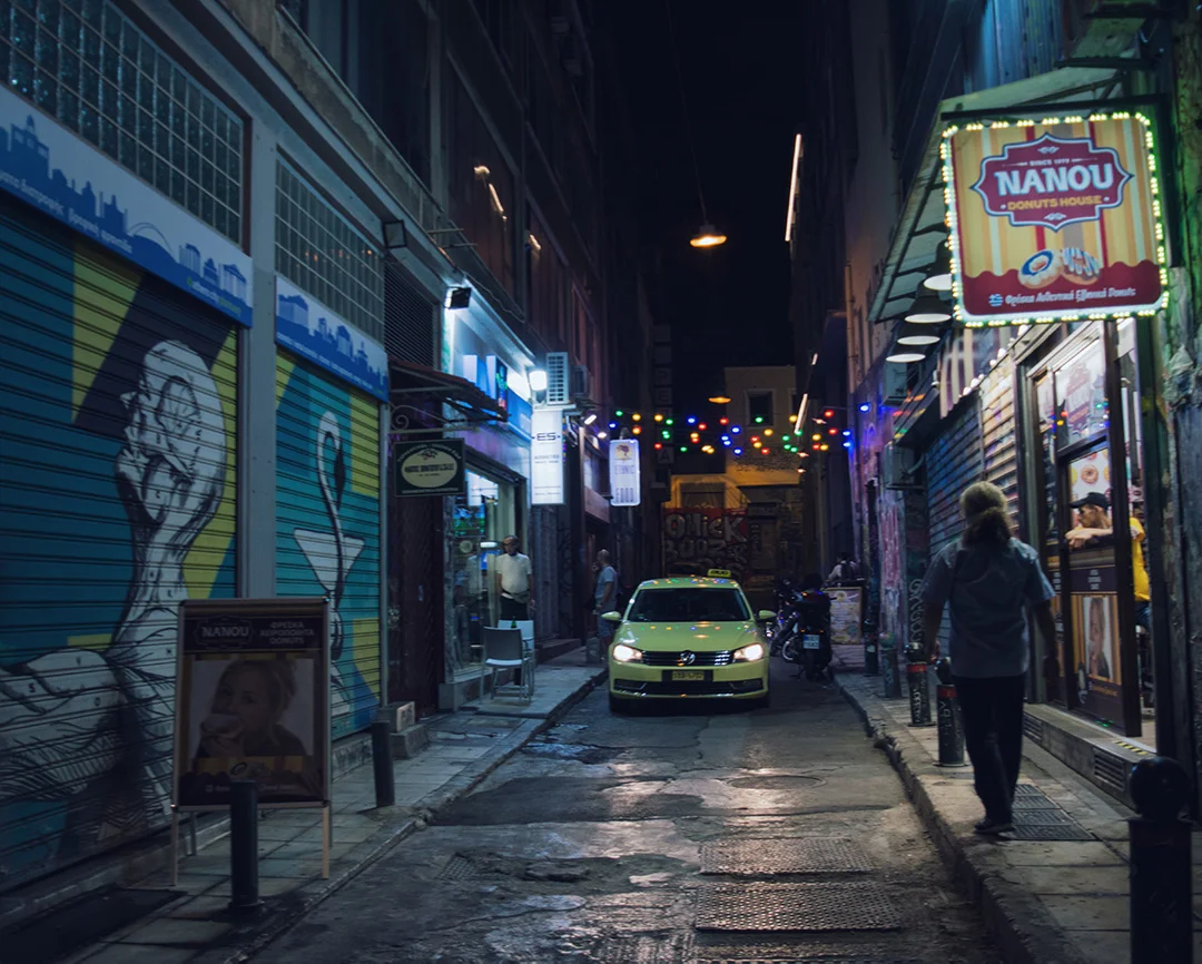 Street in Athens at night with graffities, a taxi and a man outside a Nanou donut shop